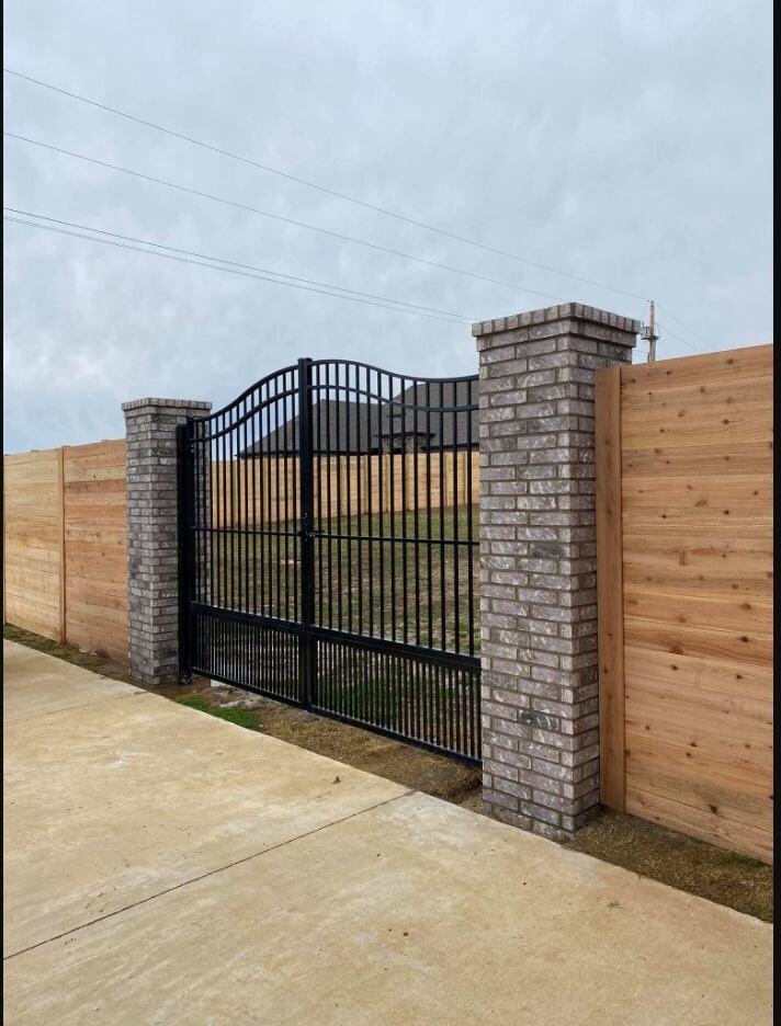 Black ornamental driveway gate between brick columns
